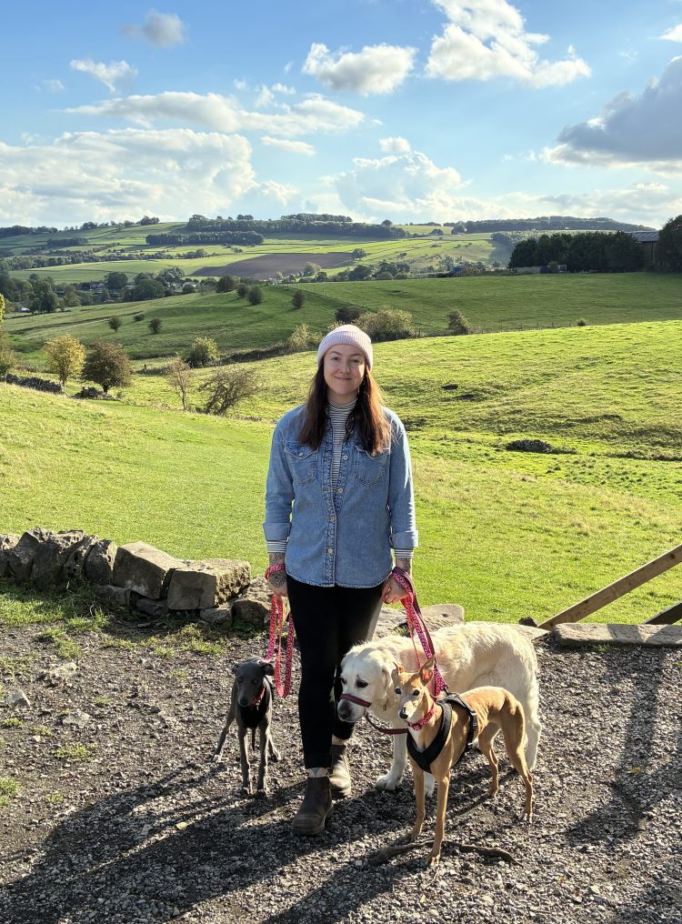 C.E.A Dog Grooming with her three dogs in the countryside surrounded by blue skies and green hills.